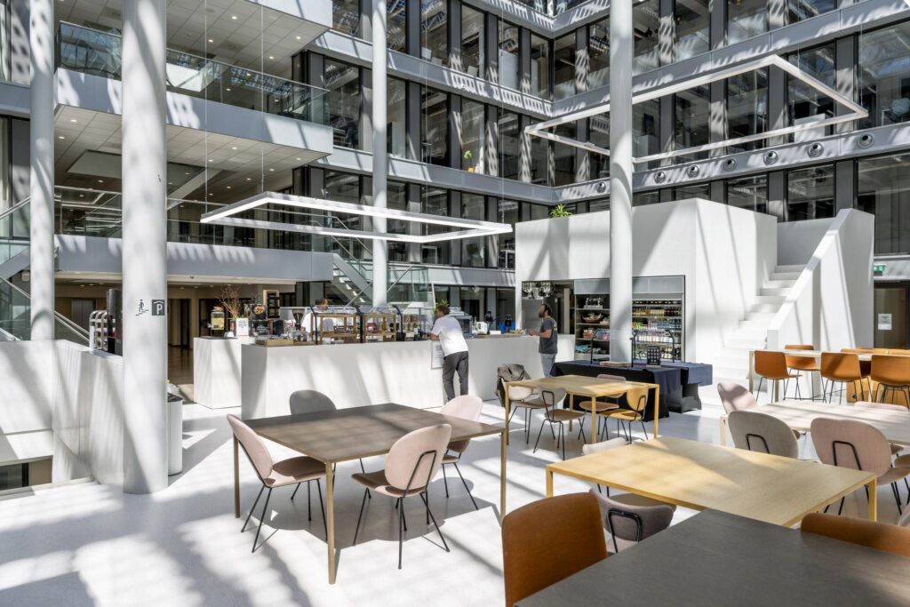 Modern indoor café area with tables, chairs, and a counter inside a bright office building on Mr. Treublaan.
